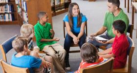 young male counselor meets with small elementary class in library
