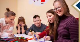 image of teacher helping students with an art project; one student smiles at the camera