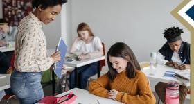 Teacher smiles and looks down to review work on middle school student's desk