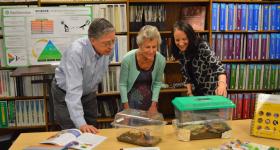 Dr. Carol O'Donnell, Douglas M. Lapp and Anne B. Keiser stand in a classroom, leaning over some desks with clear animal crates on them."