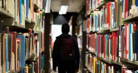 student walks through the aisle of library shelves filled with books